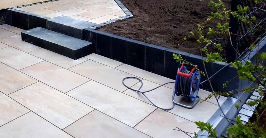 Terrasse mit hellen Feinsteinplatten und dunkler Palisadenkante